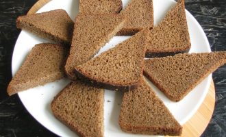 Черный хлеб (идеально подойдет бородинский или здоровье) нарежьте на прямоугольные кусочки, толщиной не более одного сантиметра. А потом разделите пополам, чтобы получились форма треугольника.