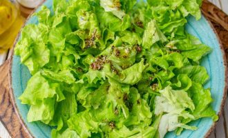На сервировочное блюдо порвите листья салата и полейте 1/3 части заправки.