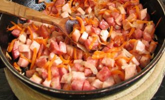 Обжарьте колбасу, морковь и лук до легкого колера.