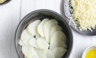 Выложите первый слой картофеля, формируя спираль и следя за тем, чтобы дно формы было полностью покрыто