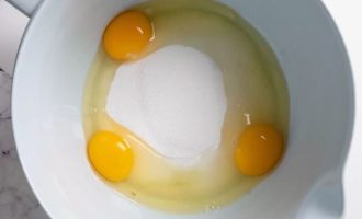 В большую миску разбейте яйца, всыпьте сахар-песок и взбейте до загустения.