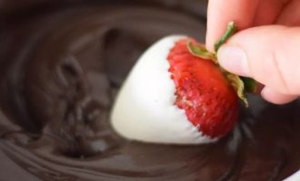 Как только белый шоколад полностью застынет на ягодах, возьмите одну ягоду и окуните ее в темный шоколад под углом 45 градусов, чтобы шоколад покрыл одну сторону ягоды по диагонали.