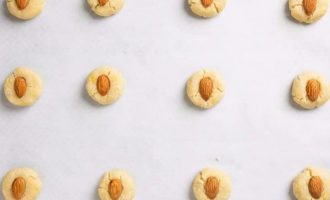 Ядра миндального ореха подсушите на сухой сковородке, охладите и выложите в продавленную пальцем серединку каждого печенья.