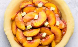 Достаньте тесто для пирога из холодильника и залейте смесью персиковой начинки - добавьте нарезанное сливочное масло.