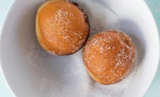 Обваляйте пончики в сахаре, пока они теплые.
