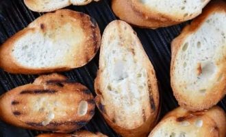 Щедро смажьте нарезанный батон или хлеб оливковым маслом и обжарьте на сковороде-гриль на среднем огне, пока он не подрумянится