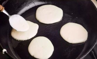 Далее смажьте толстостенную сковородку растительным маслом, выложите ложкой тесто похожее на кружочки и поджарьте в течение двух минут. За это время на поверхности будут появляться пузырьки.