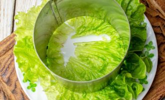Листья салата промойте под струей холодной воды, на тарелку выложите аккуратно листья салата, на них установите кулинарное кольцо.