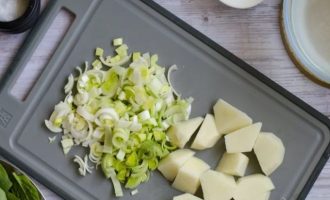 Далее вымойте 300 г шпината и 100 картофеля, нарежьте 100 г лук-порей, очистите и нарежьте 1 картофелину на небольшие кусочки, а лук (белую часть) нашинкуйте в виде полуколец