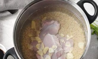 Добавьте в кастрюлю рис, куриные бедра, имбирь, чеснок и влейте воду
