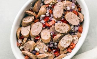 Добавляем в кастрюлю нарезанную дольками немецкую колбаску, репчатый лук, болгарский перец, чеснок, тмин