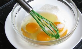 В миску вбейте яйца, всыпьте сахар, соль и все хорошо пробейте с применением ручного венчика.