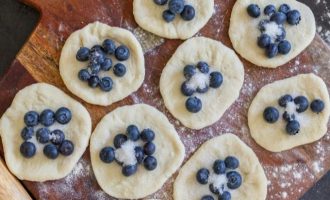 Каждый кусочек тестовой заготовки раскатайте в тонкую лепешку. Чернику вымойте, просушите и выложите на середину теста, сверху посыпьте сахаром.