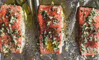 Выложите нарезанные филе лосося кожей вниз на подготовленный противень и равномерно распределите смесь чеснока и петрушки.